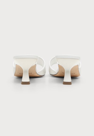 Paire de sandales blanches à bouts ouverts avec talons blocs moyens et brides simples sur les orteils, vues de dos sur un fond neutre.