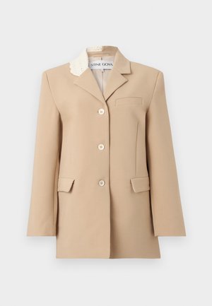 Béžové jednorzadové sako s tromi gombíkmi, dvoma prednými vreckami s klopou, náprsným vreckom a bielym čipkovým detailom na jednom klopovom golieri.