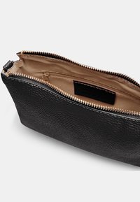 Borsetta in pelle nera con finitura testurizzata, zip dorata e foderato interno beige. Presenta una piccola tasca interna per l'organizzazione.