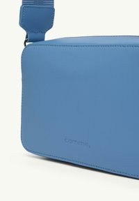 Niebieska skórzana torba o gładkiej teksturze, prostokątnym kształcie i wytłoczonym logo z boku. Posiada regulowany pasek do noszenia.