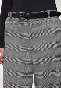 Spodnie w czarno-białą kratę w stylu houndstooth, z czarnym skórzanym paskiem z srebrną klamrą i gładką teksturą.
