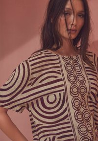 Losse beige top van textiel met een gestructureerde stof, voorzien van donkere cirkel- en lijnpatronen. Korte mouwen en een wijde halslijn.