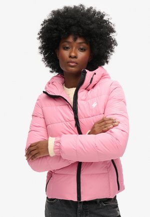 Roze pufferjack met een capuchon, voorzien van zwarte ritsen en geribde manchetten. Gequilt patroon biedt isolatie en een snug fit.