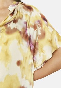 Żółta i kremowa bluzka z wzorem tie-dye w odcieniach brązu i fioletu, z krótkimi rękawami i miękką, lejącą się teksturą materiału.