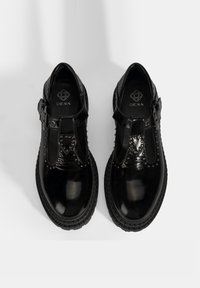 Zwarte lakleren schoenen met een T-bandontwerp, decoratieve studs, een gevoerde binnenzool en een dikke rubberen zool. Merkenlogo zichtbaar aan de binnenkant.