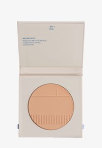 Poudre compacte dans un étui carré. Couleur beige clair avec une surface texturée. Étiquette à l'intérieur indiquant les ingrédients en texte bleu.