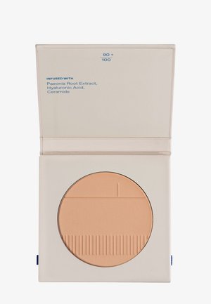 Compact powder in a square case. Light beige color with a textured surface. Label on the inside lists ingredients in blue text.