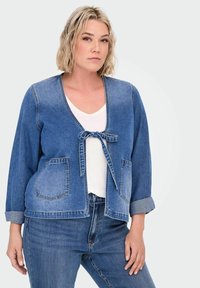 Jeans jakna z vezanim sprednjim delom, širokimi rokavi in dvema sprednjima žepoma, v srednje modri barvi, nosi se preko bele majice in usklajenih modrih kavbojk, teksturirana tkanina.
