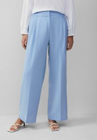Lichtblauwe wijde broek met voorplooien, gemaakt van gladde stof, gecombineerd met witte hakken met banden. Eenvoudig en modern design.