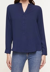 Blouse bleu marine à manches longues avec un décolleté en V et une patte de boutonnage. Tissu doux, coupe décontractée et manches à poignets. Texture lisse sans motifs.