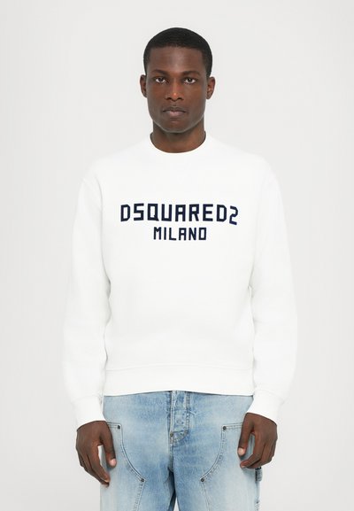 White sweatshirt with navy "DSQUARED2 MILANO" text, crew neckline, and ribbed cuffs and hem, paired with light blue jeans.