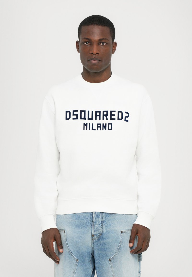 Valge sviiter, millel on sametiselt sinine "DSQUARED2 MILANO" tekst, ümar kaelus ning soonikkoes varrukate ja äärega, koos helesiniste teksadega.