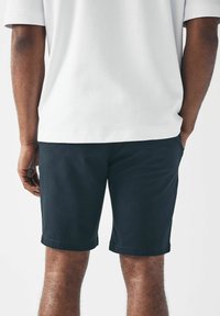Pantalones cortos de algodón negro con un ajuste entallado y dobladillo enrollado, combinados con una camisa blanca de manga corta que muestra una textura suave.