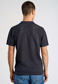 Mörkblå kortärmad polo med nättextur, med en ribbad krage och mudd, som visar en ventilerande design och diskreta detaljer.