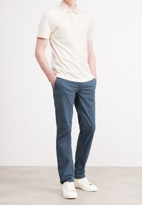 Ljusbeige pikétröja med krage, kombinerad med marinblå byxor. Outfitten kompletteras med vita sneakers. Platt textur, avslappnad design.