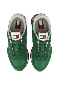 Sneakers verdi con una texture liscia, design a strati, lacci bianchi e suola nera. Presentano una toppa con logo in rosso, bianco e blu sulla linguetta.
