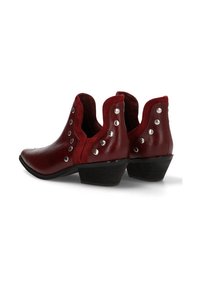 Botines de cuero rojo hasta el tobillo con punta afilada, bordes festoneados, tachuelas plateadas a los lados y un tacón bajo apilado. Acentos de ante texturizado.