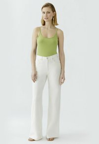 Grünes, eng anliegendes Tanktop und weiße, weite Jeans. Der Stoff wirkt glatt mit minimalen Nähten. Sandalen mit einem schlichten Design werden getragen.