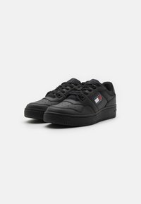 Sneakers in pelle nera con una texture liscia, punta rotonda, design con lacci e una piccola etichetta logo con strisce rosse, bianche e blu sul lato.