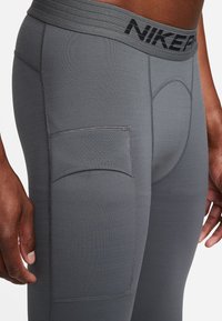 Leggings atléticos grises con una tela texturizada, que cuentan con una cintura reforzada y un bolsillo lateral. Detalles de costura visibles en las costuras.