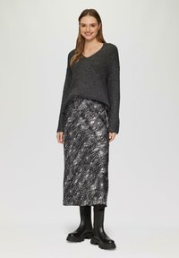 Donkergrijze gebreide sweater met een V-hals en lange mouwen, gecombineerd met een zwarte midi-jurk met slangpatroon en chunky zwarte enkellaarsjes.