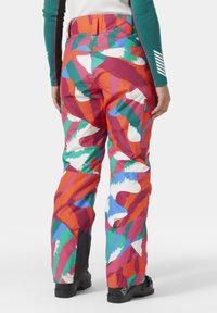 Pantalones de esquí coloridos con un patrón abstracto en rojo, verde, naranja y blanco. Fabricados con material duradero y con piernas inferiores reforzadas en negro.