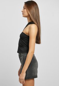 Musta crop-top yhdellä olalla, yhdistettynä korkeavyötäröisiin harmaisiin farkkuhameeseen. Sujuva kangas ja vartalonmyötäinen leikkaus.