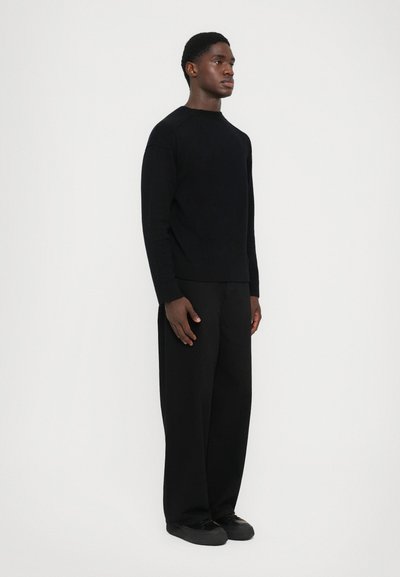 Black knit sweater with a crew neck and ribbed cuffs paired with wide-leg black trousers. Minimalistic design with a smooth texture.