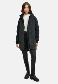 Lång huva jacka med en texturerad mörkgrå fleeceframsida och svarta quiltade ärmar, som har två zip-fickor och en framslupp med dragkedja.