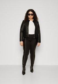 Black faux leather jacket with a fitted design, paired with high-waisted black leggings and pointed ankle boots. White shirt underneath.