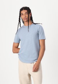 Camiseta de manga corta azul claro, hecha de una tela suave, con un cuello redondo y un corte relajado. Combinada con pantalones sueltos de color claro.