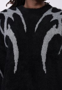 Črni pleteni pulover z puhasto teksturo, ki na sprednji strani prikazuje izrazite sive vzorce v obliki plamenov v kontrastnem dizajnu.