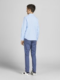 Chemise à manches longues bleu clair, pantalon marine, baskets blanches avec accents noirs et rouges, vues de l'arrière, mettant en avant un design minimaliste.
