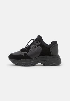 Czarne masywne sneakersy z mieszanymi panelami ze skóry i zamszu, grubą teksturowaną podeszwą oraz zamknięciem na sznurówki, pokazane z boku na jasnym tle.