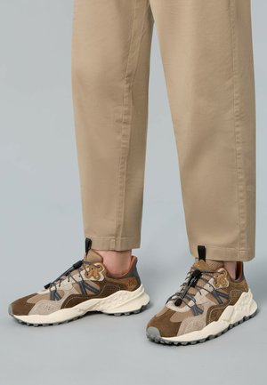 Braune und beige Sneaker bestehen aus einer Mischung aus Wildleder und Mesh-Materialien, mit einer strukturierten Sohle, elastischen Schnürsenkeln und einem braunen Akzent an der Ferse.