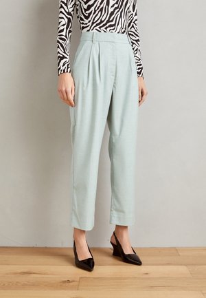Femme portant un pantalon bleu clair taille haute et fuselé, associé à des escarpins noirs à bout pointu et un haut à manches longues imprimé zèbre.