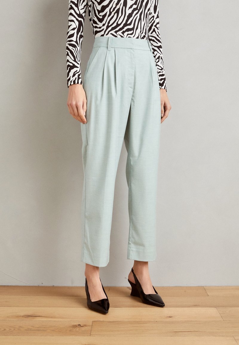 Femme portant un pantalon bleu clair taille haute et fuselé, associé à des escarpins noirs à bout pointu et un haut à manches longues imprimé zèbre.