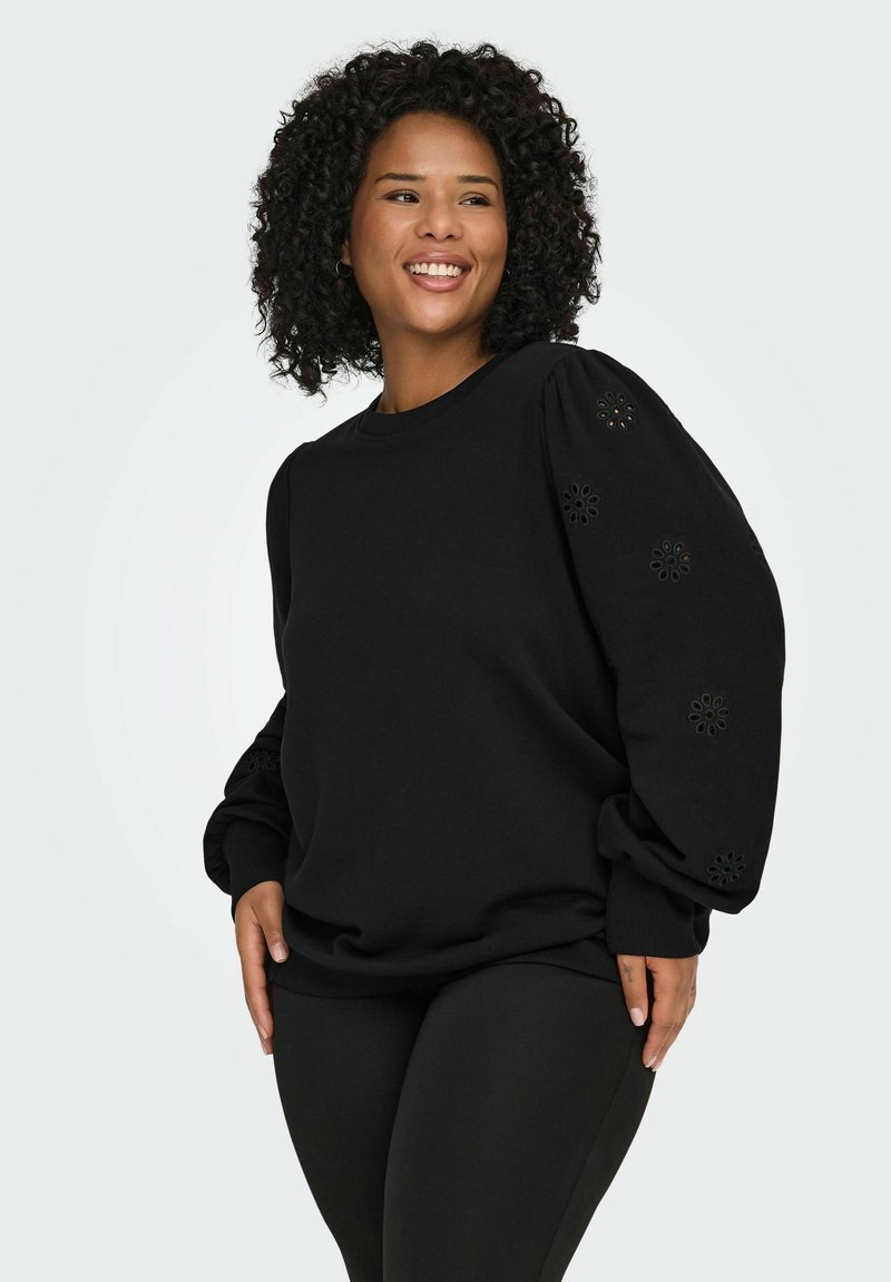 Črna majica s kapuco z okroglim izrezom, rebrastimi manšetami in okrasnimi izrezanimi cvetličnimi vzorci na rokavih. Mehka, teksturirana tkanina.