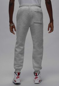 Grå sweatpants lavet af blød stof har en afslappet pasform, elastisk talje og en baglomme, parret med hvide og røde sneakers.