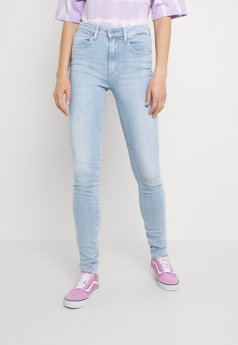 Vaqueros ajustados de color azul claro, hechos de denim con una textura suave. Presentan bolsillos delanteros y una cintura de altura media. Combinados con zapatillas de ante rosa.