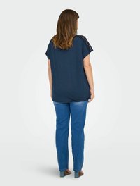 Navy blue short-sleeve top with lace detail on shoulders, paired with light blue straight-leg jeans and open-toed heels. Smooth texture.