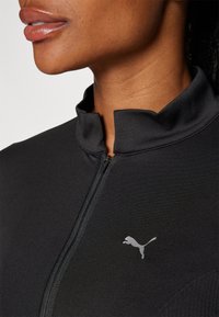 Svart atletisk zip-up topp med mock krage, i en strukturerad tyg med en liten silver Puma-logotyp på vänster bröstområde.