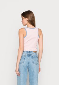 Rosa ribbad linne med blå kant, med en figurnära design och vågig nederkant. Kombinerat med högmidjade, ljusblå denimjeans.