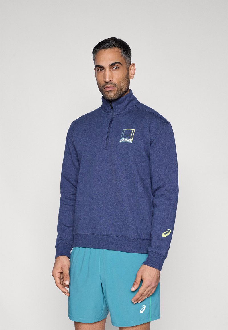 Sweat-shirt bleu marine à demi-fermeture éclair avec ourlet et poignets côtelés, comportant un logo sur la poitrine et un accent de couleur plus claire sur la manche.