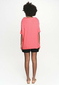 Różowy oversize'owy t-shirt o luźnym kroju, krótkich rękawach, okrągłym dekolcie i miękkiej teksturze, w połączeniu z czarnymi szortami.