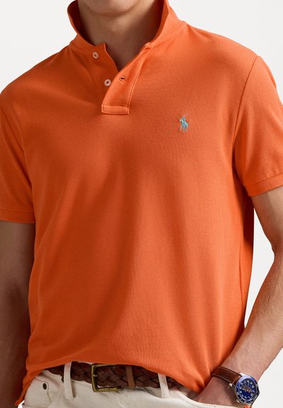 Kortärmad orange pikétröja med krage, två-knappsstängning och broderad blå logotyp på vänster bröst. Texturerad tyg.