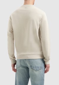 Lichtbeige sweatshirt van textuurstof, met een ronde hals en geribbelde manchetten. Gecombineerd met lichtblauwe spijkerbroeken.