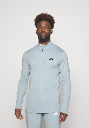 Hellblaues langärmliges Sportshirt mit hohem Kragen, Reißverschluss und schwarzem Adidas-Logo. Glattes Material mit schmalem Schnitt.