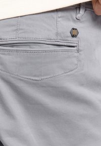Grijze stoffen shorts met een achterzak met een hexagonaal zwart metalen accent en stikdetails. Zachte textuur, eenvoudig ontwerp.