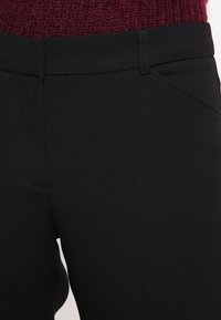 Černé kalhoty s hladkým povrchem, ve slim fit střihu, s poutky na opasek a bočními kapsami. Vyrobeny z odolné textilní směsi.